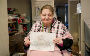 A woman holding a picture she drew at a skilled nursing nursing home facility