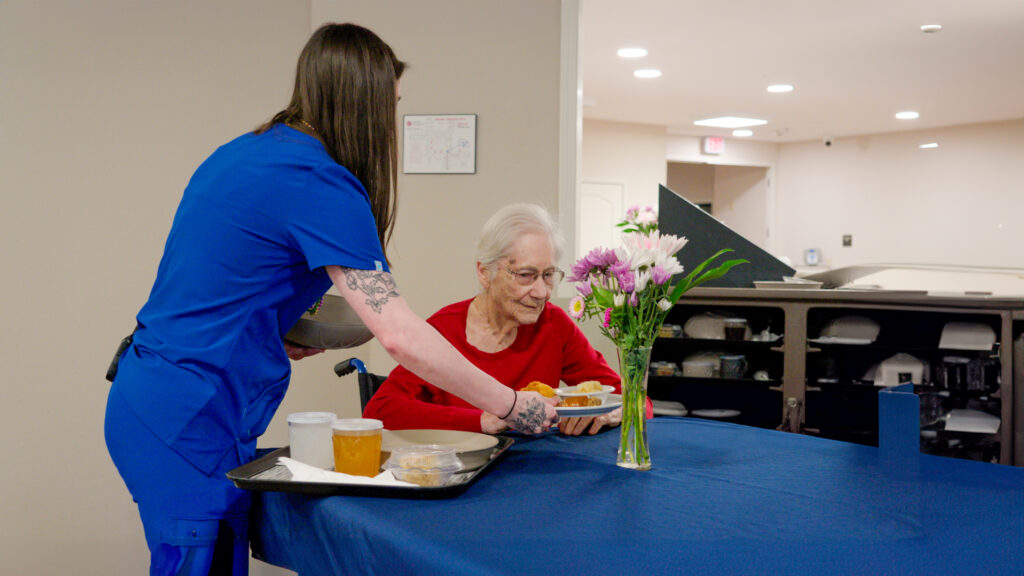 A nurse assist a woman during lunch at a long term care facility